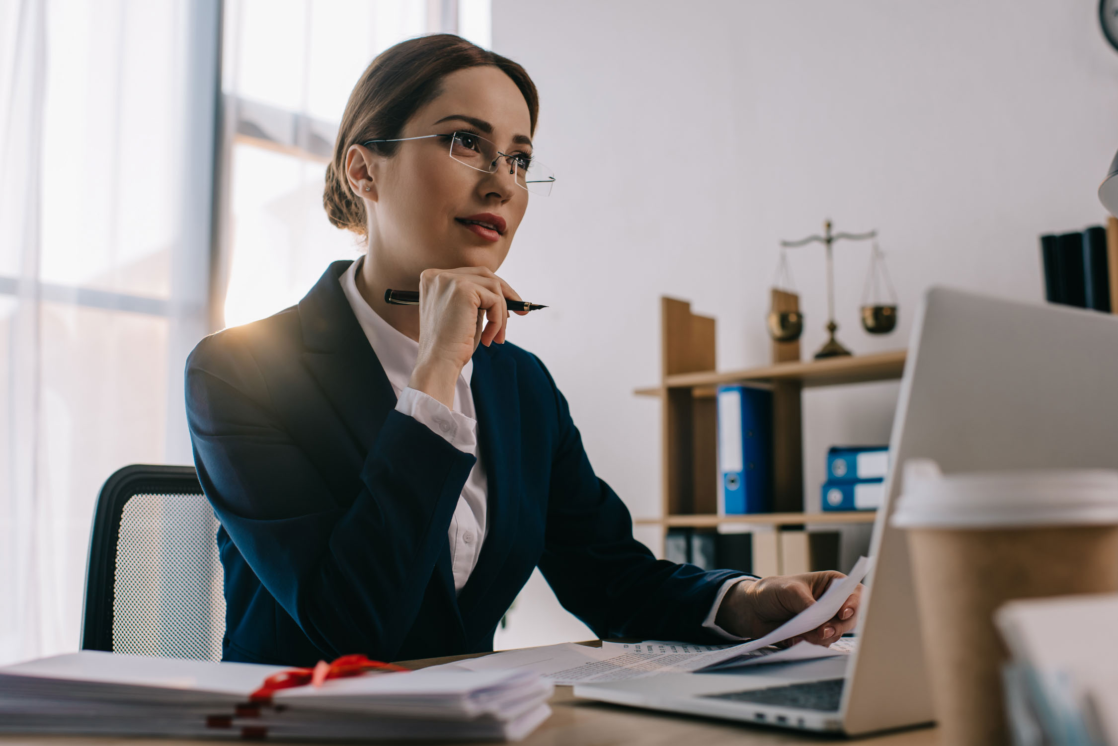 female lawyer in eyeglasses at workplace with documents and lapt